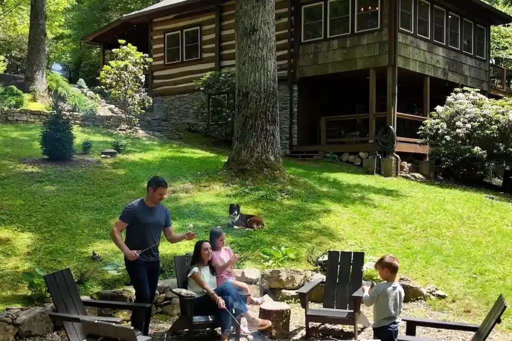 Family making s'mores at the fire pit at Hemlock Hill Cabin in Blowing Rock NC with log cabin in background